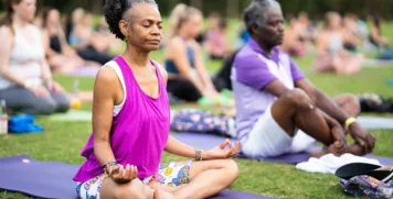 A group of people practicing mindfulness and meditation on yoga mats in an outdoor park setting, highlighting community wellness and holistic health practices.