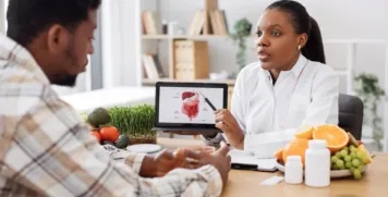 Functional medicine doctor pointing to a gut health diagram on a tablet during a patient consultation with fresh food and supplement bottles on the table.