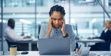 Overwhelmed woman holding her temples while experiencing brain fog at office desk