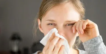 Woman wiping her nose with a tissue and rubbing her watery eyes due to nasal allergy symptoms