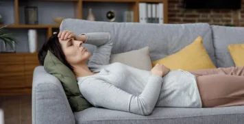 Exhausted woman resting on a sofa holding her head, illustrating chronic fatigue as an early sign of autoimmune disease.